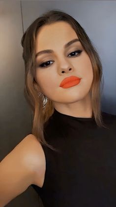 a woman with orange lipstick on her face and black dress, standing in front of a mirror