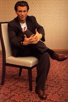 a man in a suit sitting on a chair with his legs crossed and hands folded