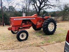 an old red farmall tractor parked on the side of a road next to a tree