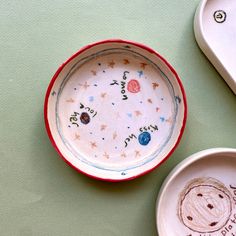 two bowls with designs on them sitting next to spoons and plates that have writing on them