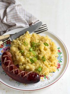 a hot dog on a plate with mashed potatoes and green onions next to a fork