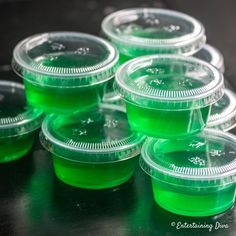 green plastic cups are lined up on a black countertop, ready to be filled with liquid