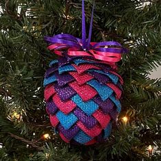 a pine cone ornament hanging from a christmas tree with purple and blue ribbons