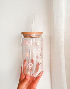 a hand holding a glass with a straw in it and flowers on the inside, against a white background