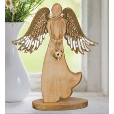 an angel figurine with a heart in its hand next to a vase filled with daisies