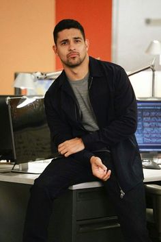 a man sitting on top of a desk in front of a computer monitor and keyboard