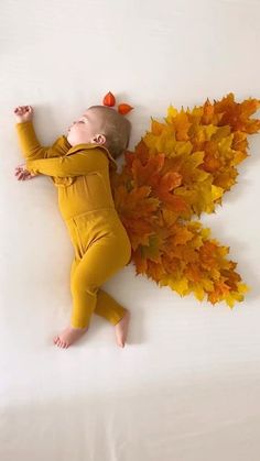 a baby is laying on its back next to some yellow and orange leaves in the shape of an angel