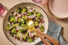 a bowl filled with broccoli and onions on top of a table next to two glasses