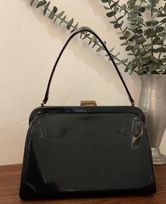 1950s 1960s Morris Moskowitz Black Patent Leather Vinyl Top Handle Handbag, Vintage Kelly Purse, Mid Century Accessory Chic 1950s 1960s black patent leather vinyl handbag in the Kelly style. It features a single black vinyl handle strap. Brass hardware with a thumb lift clasp closure that works well and closes tightly. Opens to a decorative fabric lining with one interior side metal zippered pocket. Stamped MM. There are protective feet on the bottom of the bag. Great vintage condition *the exterior shows signs of use with surface marks.   The lining is clean with no holes or odors.  The metal hardware shows normal signs of age. Please look carefully at the photos because they are part of the description. Measurements: Width x 9 7/8" across the bottom  Depth x 3 7/8" across the bottom  Hei Vintage Satchel Evening Bag For Parties, Vintage Evening Bag With Detachable Handle For Party, Retro Rectangular Evening Bag For Formal Occasions, Vintage Rectangular Evening Bag For Luncheon, Vintage Black Rectangular Evening Bag, Retro Rectangular Evening Bag For Vintage Fashion, Retro Black Evening Bag For Formal Occasions, Vintage Rectangular Bags For Evening, Vintage Rectangular Evening Bags