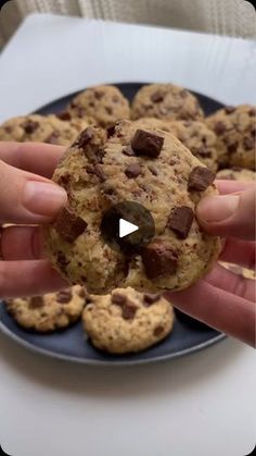 a person holding a chocolate chip cookie in front of some cookies on a blue plate