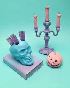 two candles, a skull head and a candle holder on a blue background with an orange pumpkin