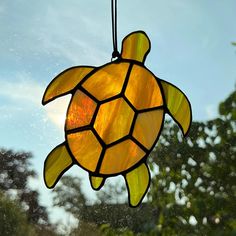 a stained glass turtle sun catcher hanging from a window sill in front of trees