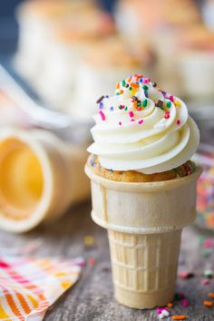 an ice cream cone with white frosting and sprinkles sits on a table