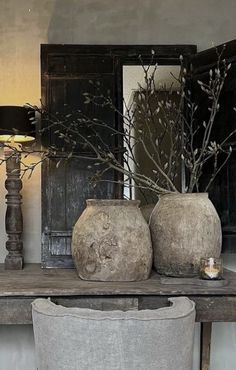 two vases sitting on top of a wooden table next to a lamp and mirror