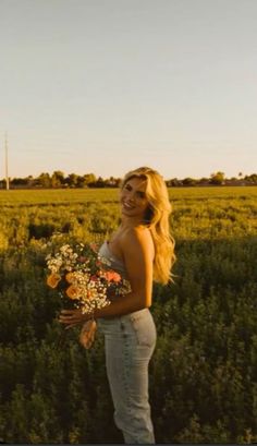 a woman standing in the middle of a field holding a bouquet of flowers and smiling