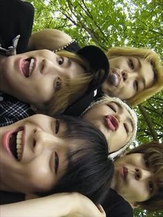 a group of young men standing next to each other in front of some trees with their mouths open