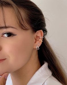 a woman with long hair wearing a white shirt and silver ear cuff earrings on her left ear