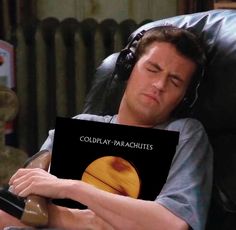 a man laying in a chair with headphones on and holding a sign that says coldplay parachutes