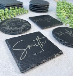 black slate coasters with handwritten names on them and green plants in the background