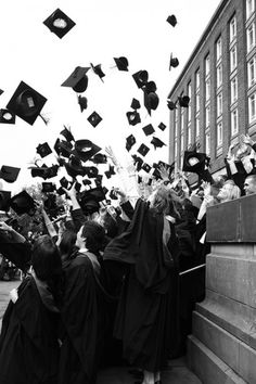 black and white photograph of graduates throwing their caps in the air at graduation ceremony on campus