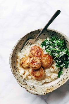 a bowl filled with rice, spinach and scallops next to a spoon