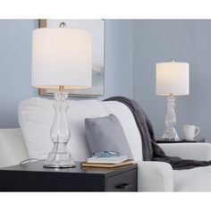 two lamps are sitting on a table next to a white couch with a gray blanket