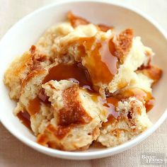 a white bowl filled with bread covered in caramel sauce on top of a table