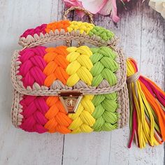 a multicolored purse sitting on top of a white wooden floor next to flowers