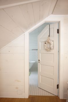 an open door leading to a bathroom with white walls and wood floors in the corner