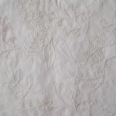 an embroidered sheet with white flowers and leaves on it