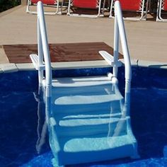 an empty swimming pool with steps leading up to the water's edge and red chairs in the background