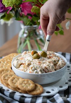 a bowl of dip with crackers and flowers in the background