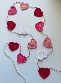 crocheted hearts hanging from string on white table with red and pink yarn around them