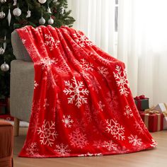 a red blanket with white snowflakes on it sitting in front of a christmas tree