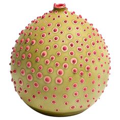 a green vase with pink dots on the top and bottom, sitting in front of a white background