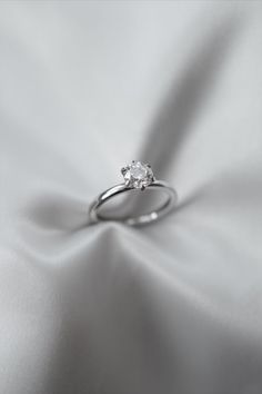 a white gold ring with a single diamond in the center on a satin fabric background