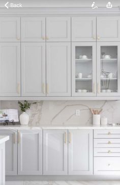 a white kitchen with marble counter tops and cabinets in front of the sink is shown