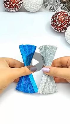 two hands are holding small pieces of blue and white paper in front of christmas ornaments