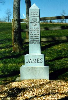 a monument in the middle of a grassy field with trees behind it and writing on it