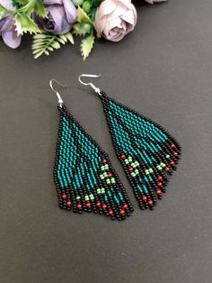 two pairs of beaded earrings sitting on top of a table next to purple flowers