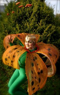 a woman in green and yellow costume with polka dots on her body, sitting next to a bush