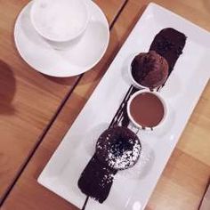 three desserts on a white plate with saucers and spoons next to each other