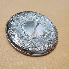 a silver pocket watch sitting on top of a wooden table next to a brown surface