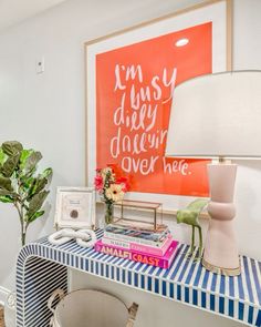 a desk with a lamp, vase and pictures on the wall in front of it