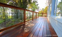 a wooden deck with glass railing and trees in the background