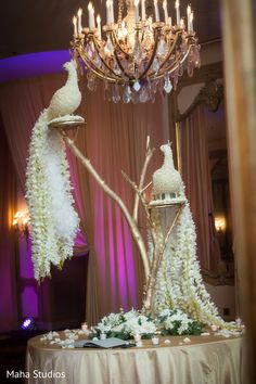 a table topped with a chandelier covered in white flowers and feathers next to a mirror