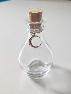 a small bottle with a cork in the top and a crescent charm hanging from it