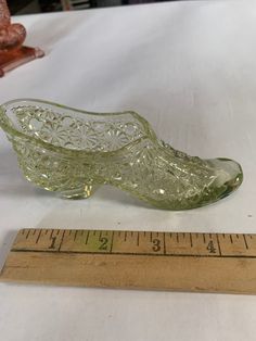 a green glass shoe sitting on top of a table next to a measuring tape,