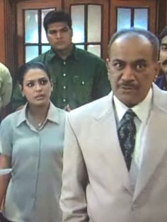 a man in a suit and tie standing next to two women with other people behind him