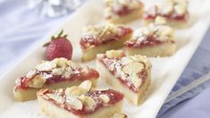 several pieces of dessert on a white plate with strawberries and almonds next to it